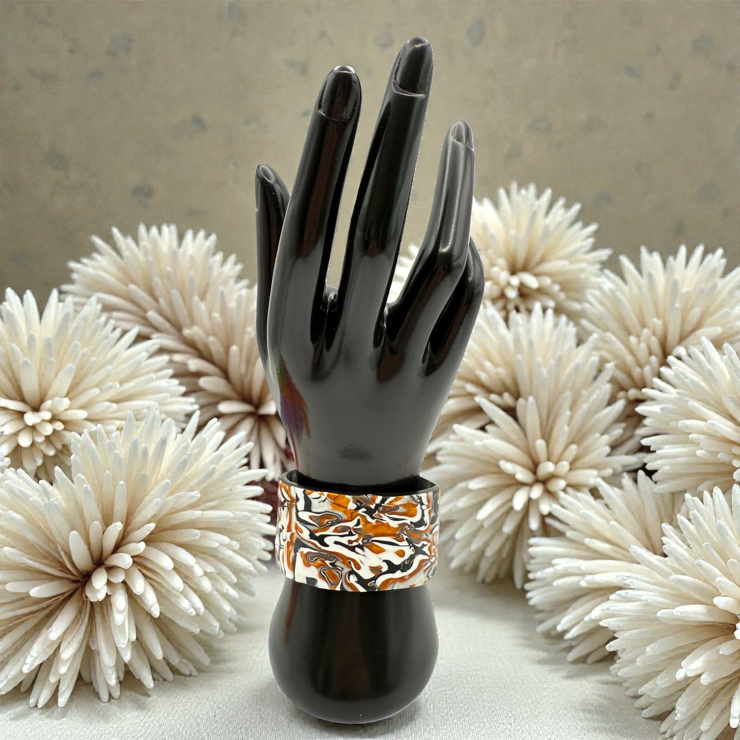 These Pretty Things Cognac Marble Cuff on a black hand mannequin with cream colour feather boas around.