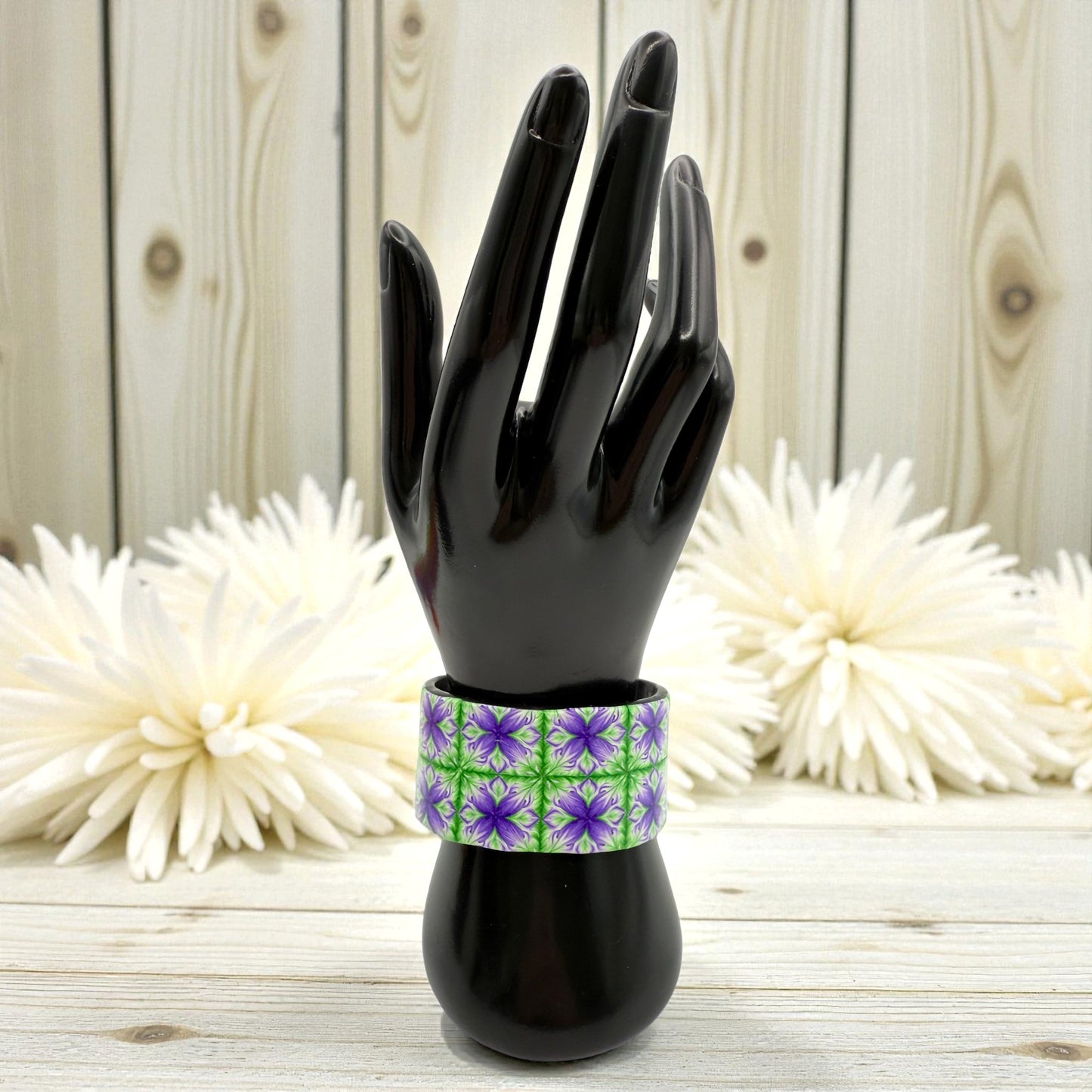 These Pretty Things Fleur De Lys Cuff on a black hand and wrist demonstraion model with a background of a white feather boa