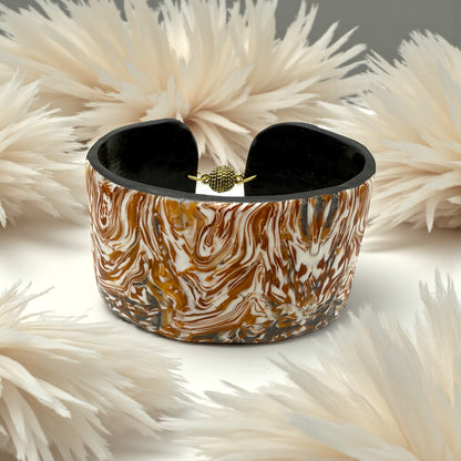 These Pretty Things Amber Swirl Cuff set in amongst a cream feather boa on a taupe colour base