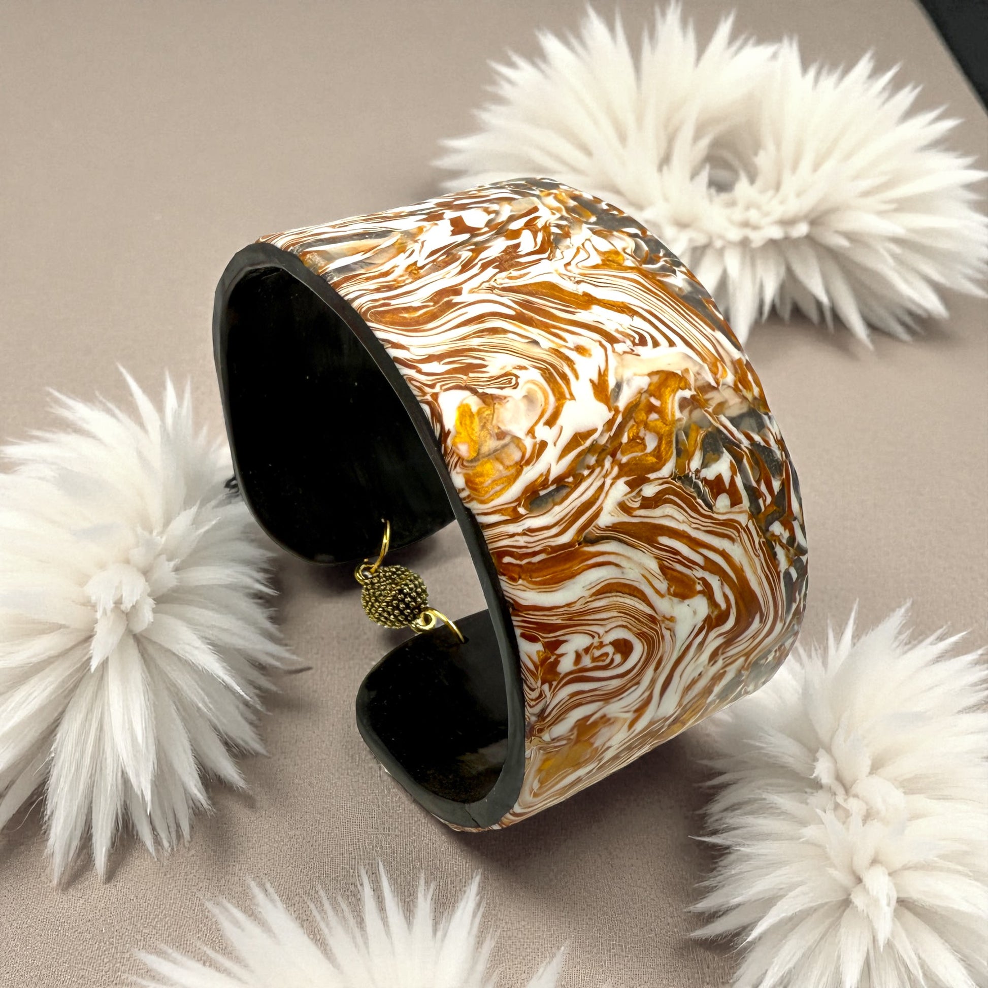 These Pretty Things Amber Swirl Cuff set in amongst a cream feather boa on a taupe colour base