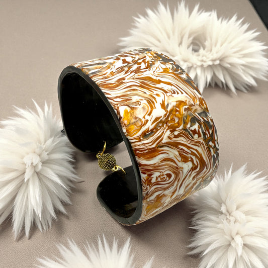 These Pretty Things Amber Swirl Cuff set in amongst a cream feather boa on a taupe colour base