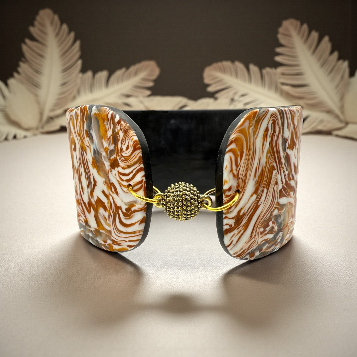 These Pretty Things Amber Swirl Cuff set in front of a cream feather boa on a cream colour table