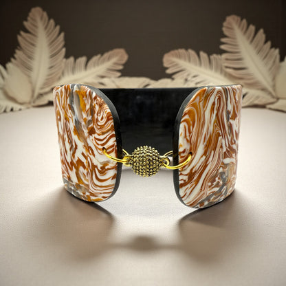 These Pretty Things Amber Swirl Cuff set in front of a cream feather boa on a cream colour table