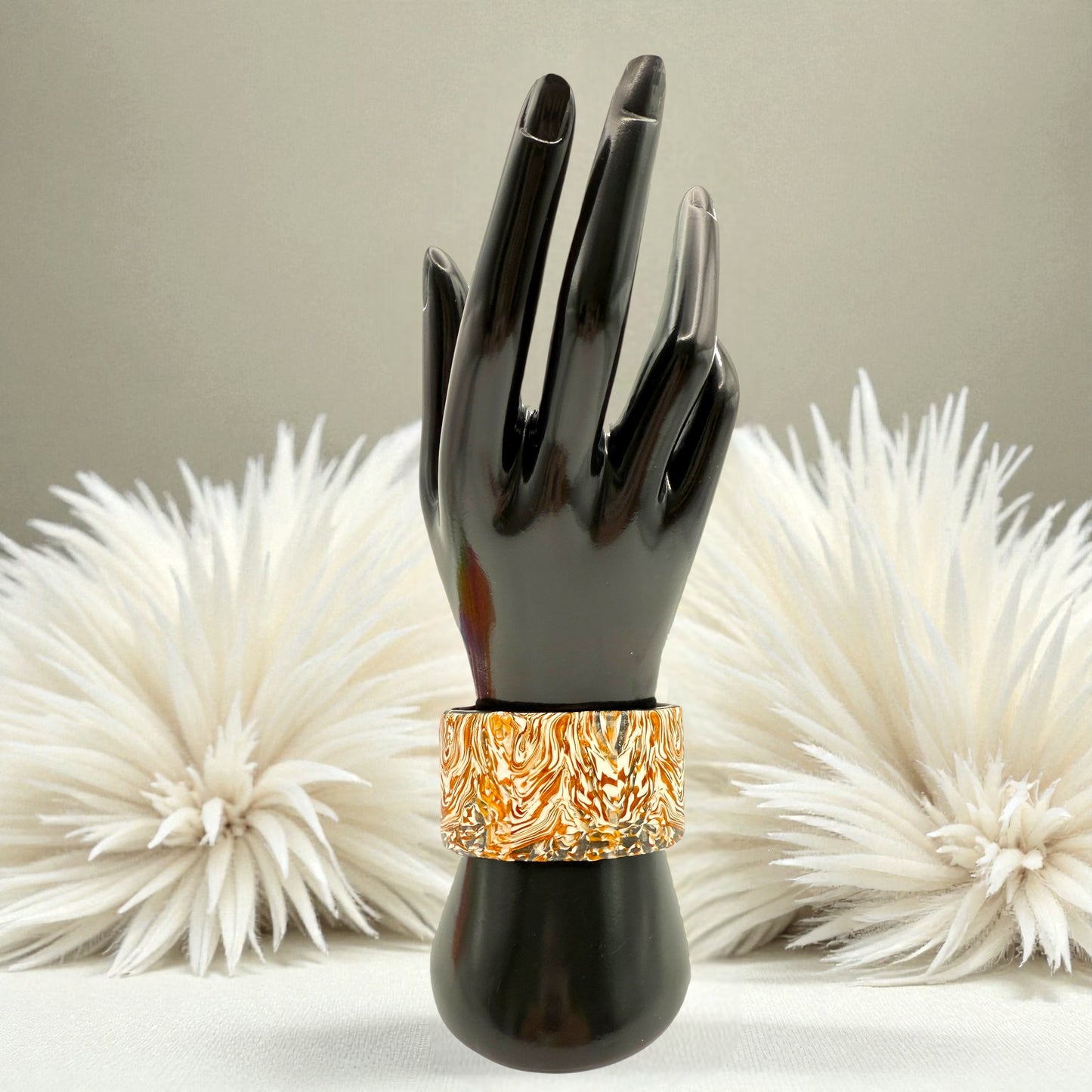 These Pretty Things Amber Swirl Cuff on a black hand mannequin set in front of a cream feather boa on a cream colour table
