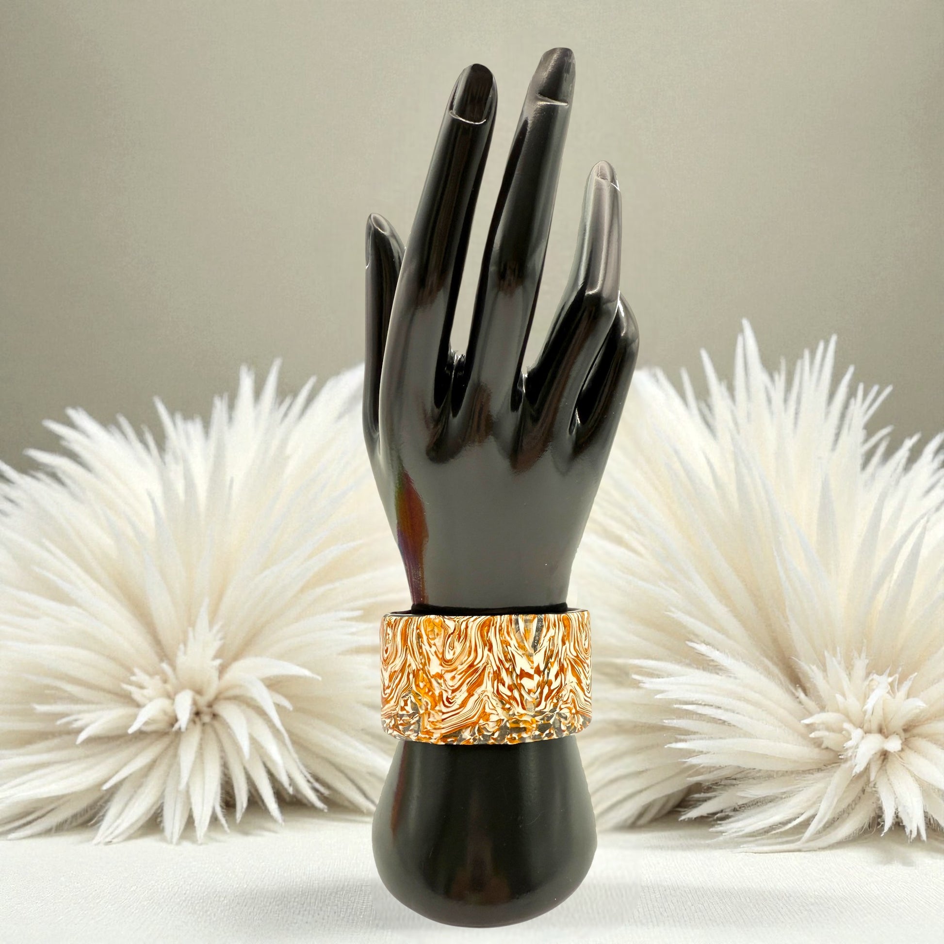 These Pretty Things Amber Swirl Cuff on a black hand mannequin set in front of a cream feather boa on a cream colour table
