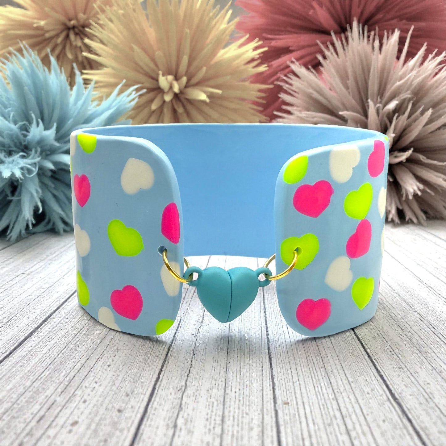 These Pretty Things Blue Fluorescent Cuff on a wood slated base with multiple coloured feather boas in the background