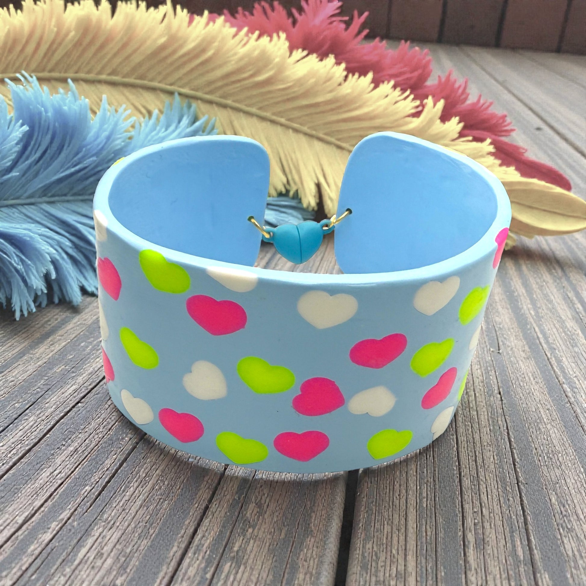These Pretty Things Blue Fluorescent Cuff on a wood slated base with multiple coloured feather boas in the background