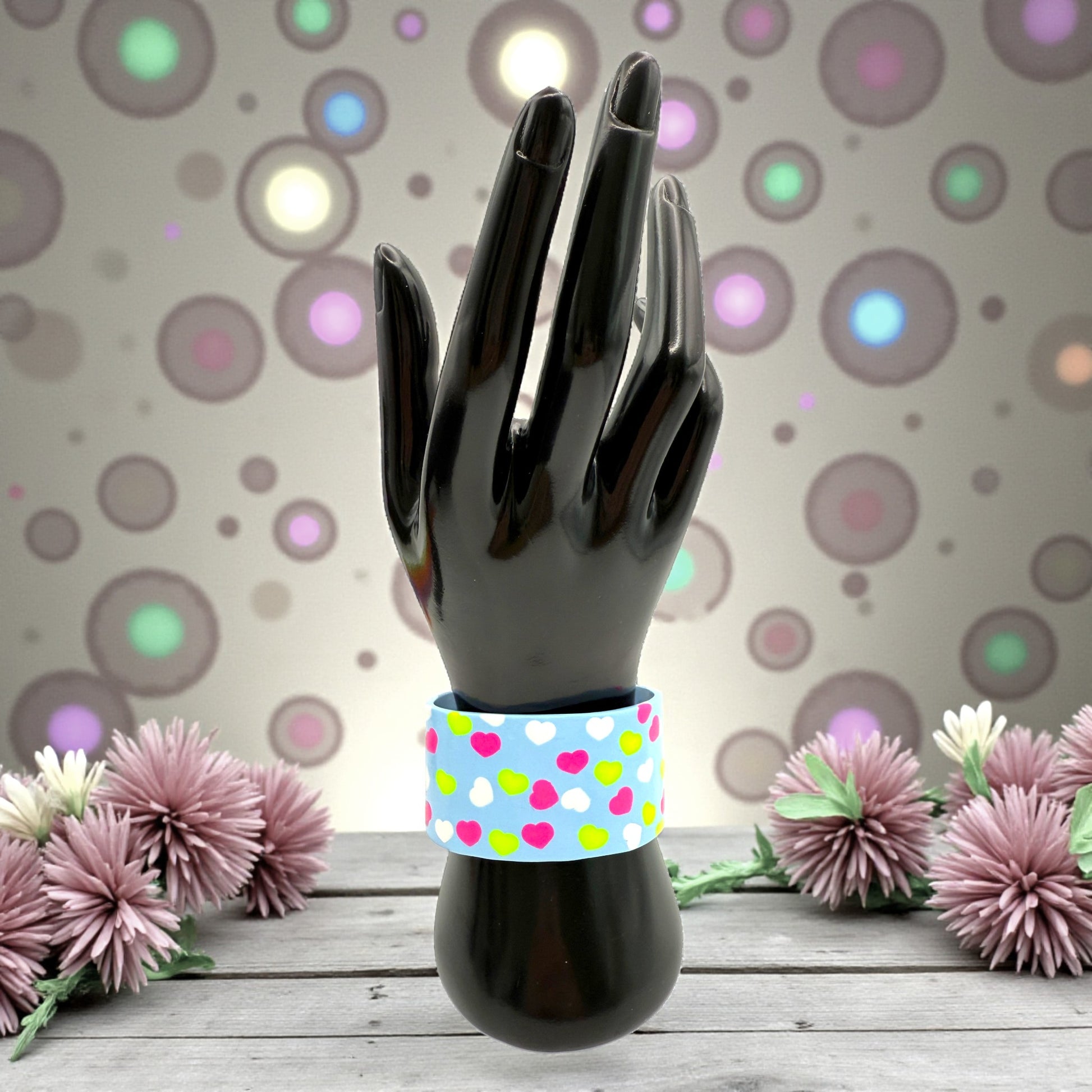 These Pretty Things Blue Fluorescent Cuff on a black hand mannequin with multiple coloured flowers in the background