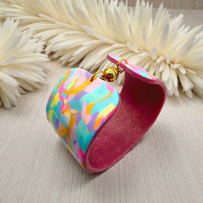 These Pretty Things Candy Cane Cuff on a table with a cream feather boa in the background