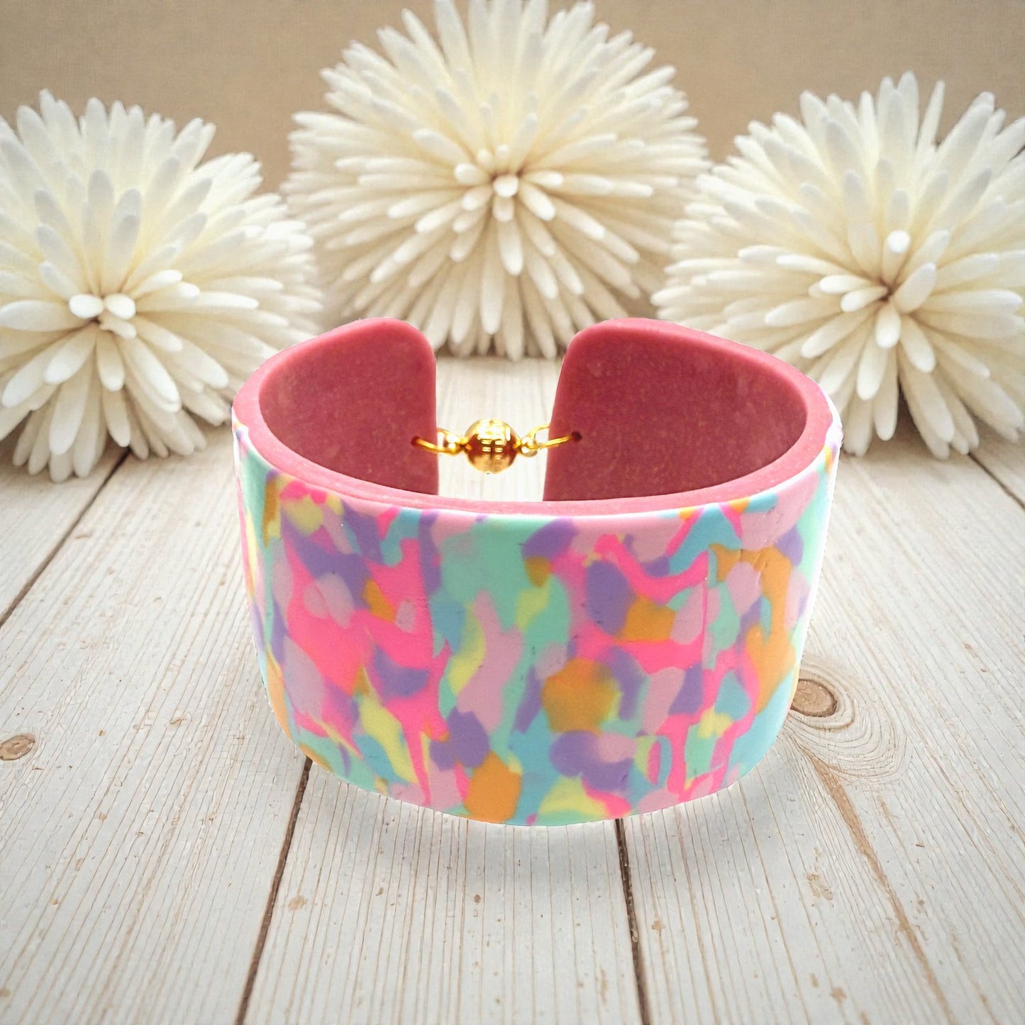 These Pretty Things Candy Cane Cuff on a table with a cream feather boa in the background