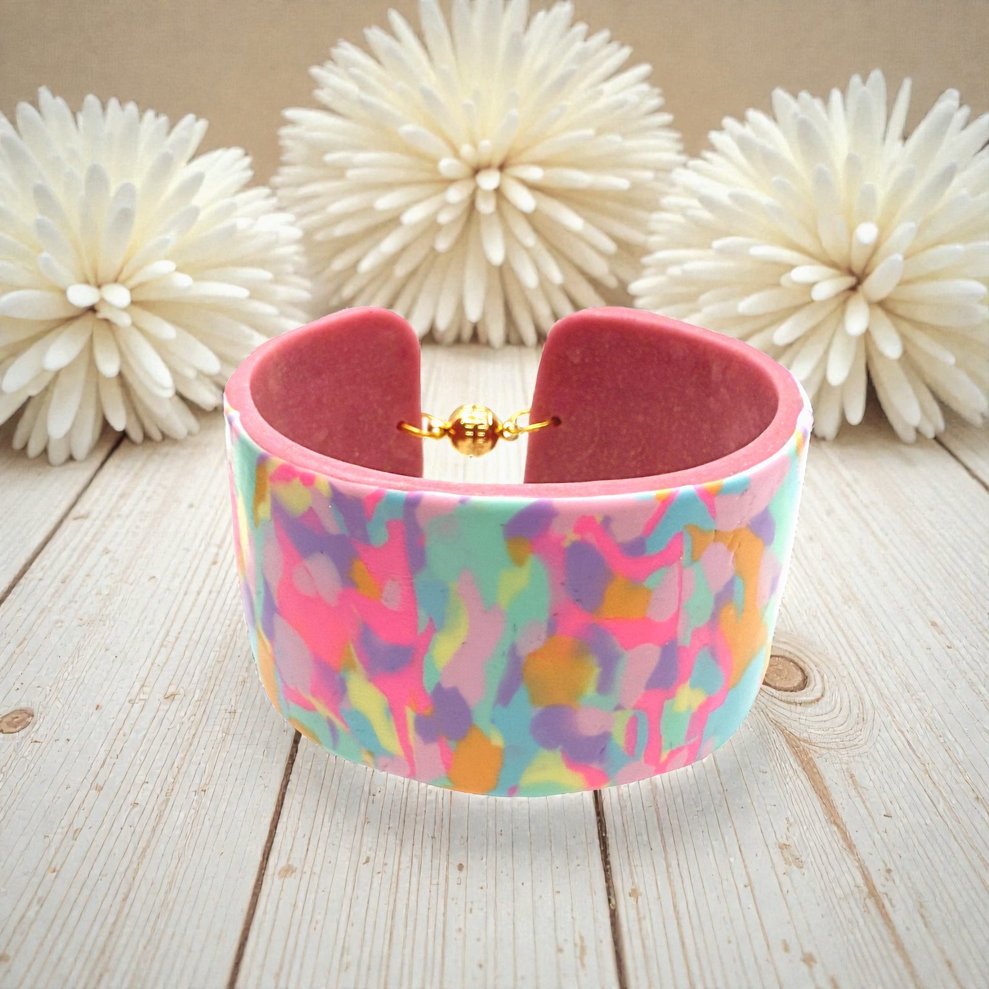 These Pretty Things Candy Cane Cuff on a table with a cream feather boa in the background