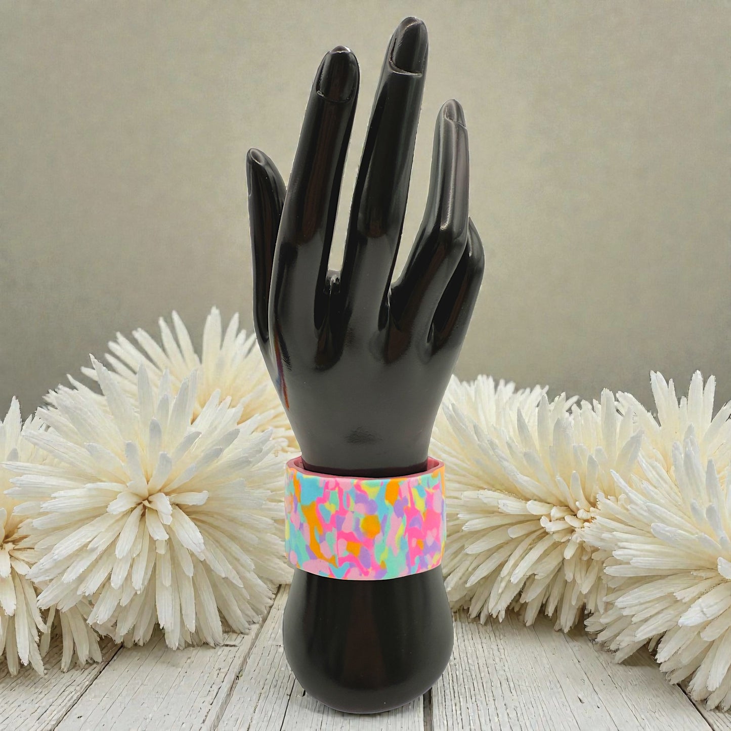 These Pretty Things Candy Cane Cuff on a black hand mannequin with a cream feather boa in the background