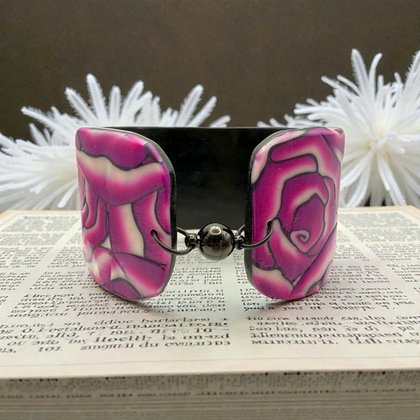 These Pretty Things Cherry Rose Cuff on a newspaper base with a cream feather boa in the background