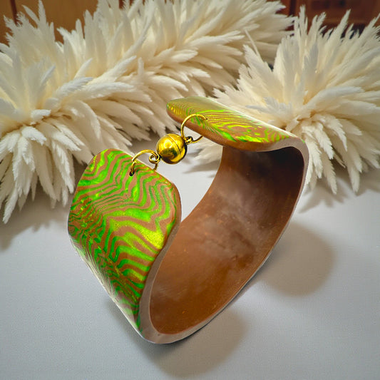 These Pretty Things Chocolate Lime Cuff on a table with a cream colour feather boa in the background