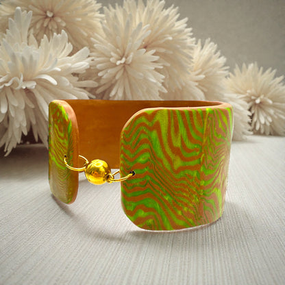 These Pretty Things Chocolate Lime Cuff on a table with a cream colour feather boa in the background