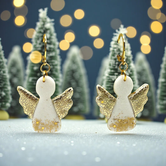Christmas Angel earrings from These Pretty Things with gold wings against a festive background with blurred lights and trees.