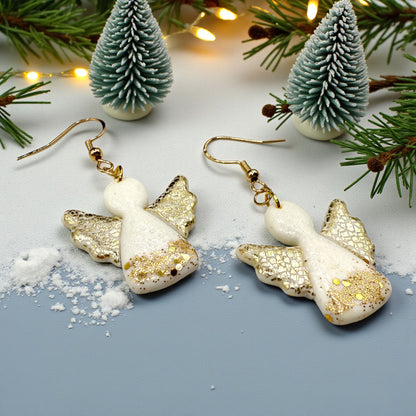 Christmas Angel earrings from These Pretty Things on a snowy surface with Christmas trees and lights in the background.