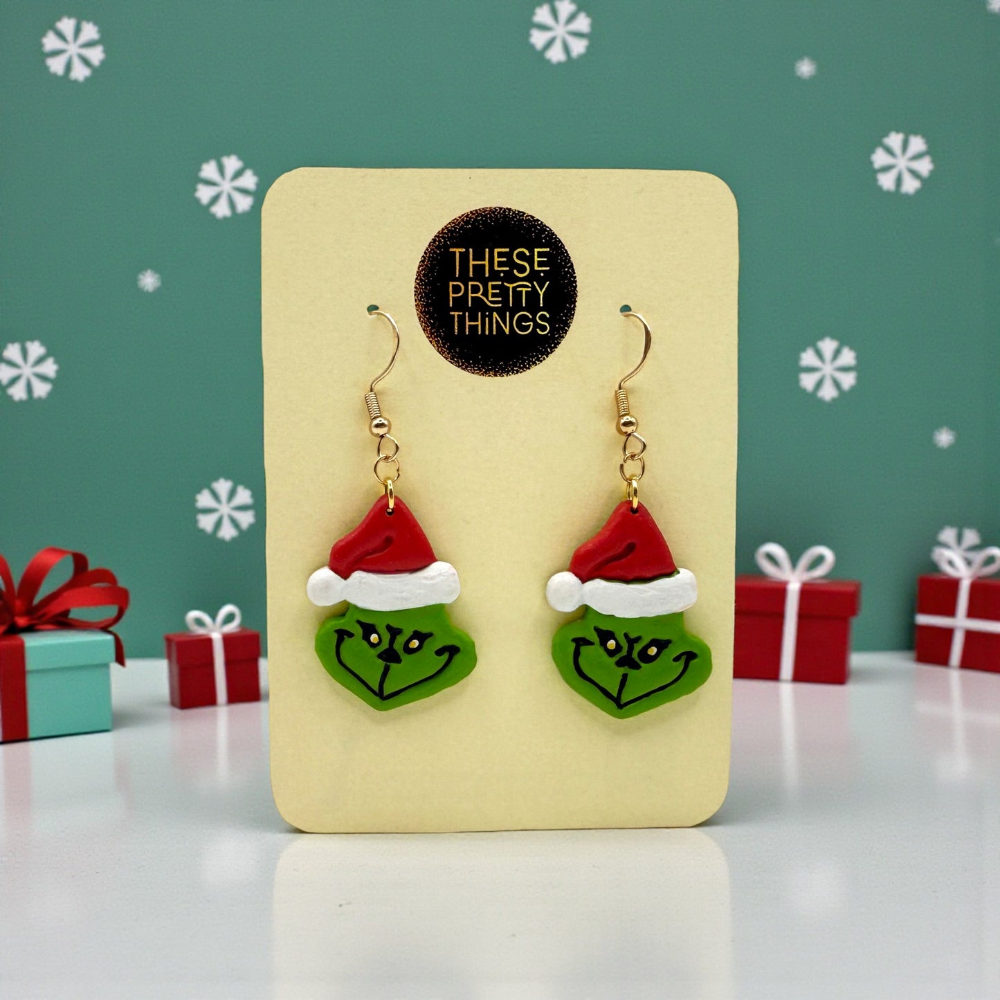 Grinch earrings on a These Pretty Things presentation card with Christmas themed background.