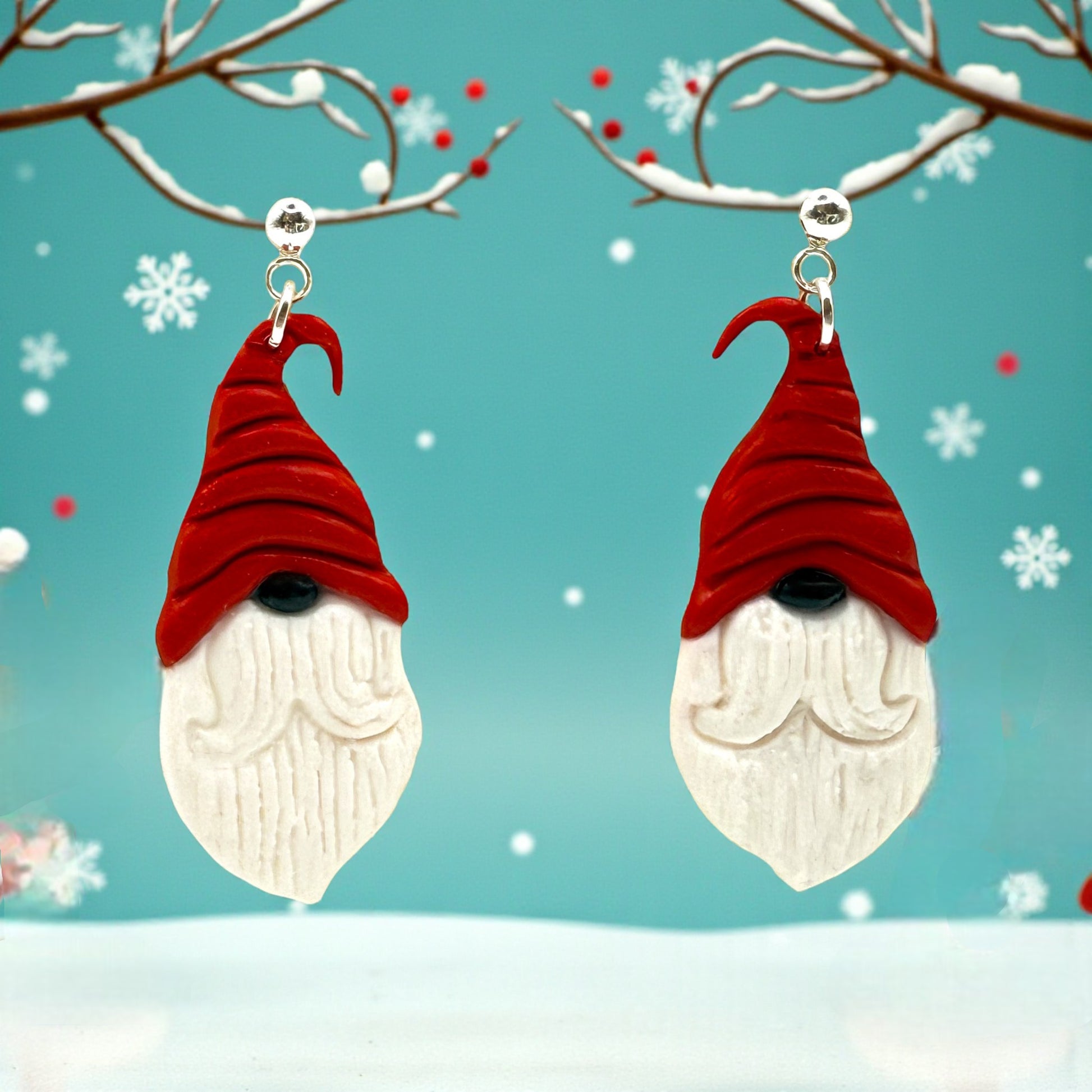 Nordic Santa earrings from These Pretty Things with red hats, black nose and white beards against a snowy background.