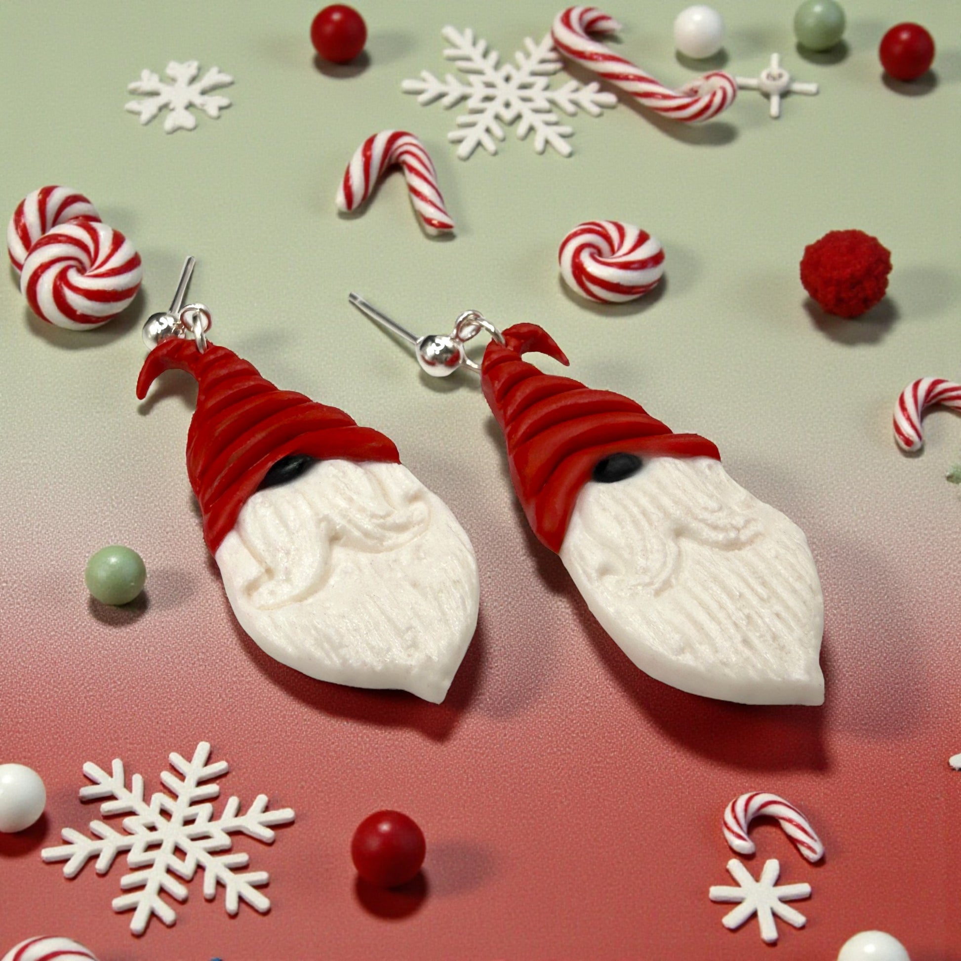 Nordic Santa earrings from These Pretty Things with red hats, black nose and white beards on a festive background with candy and snowflakes.