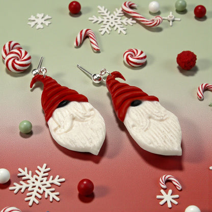 Nordic Santa earrings from These Pretty Things with red hats, black nose and white beards on a festive background with candy and snowflakes.