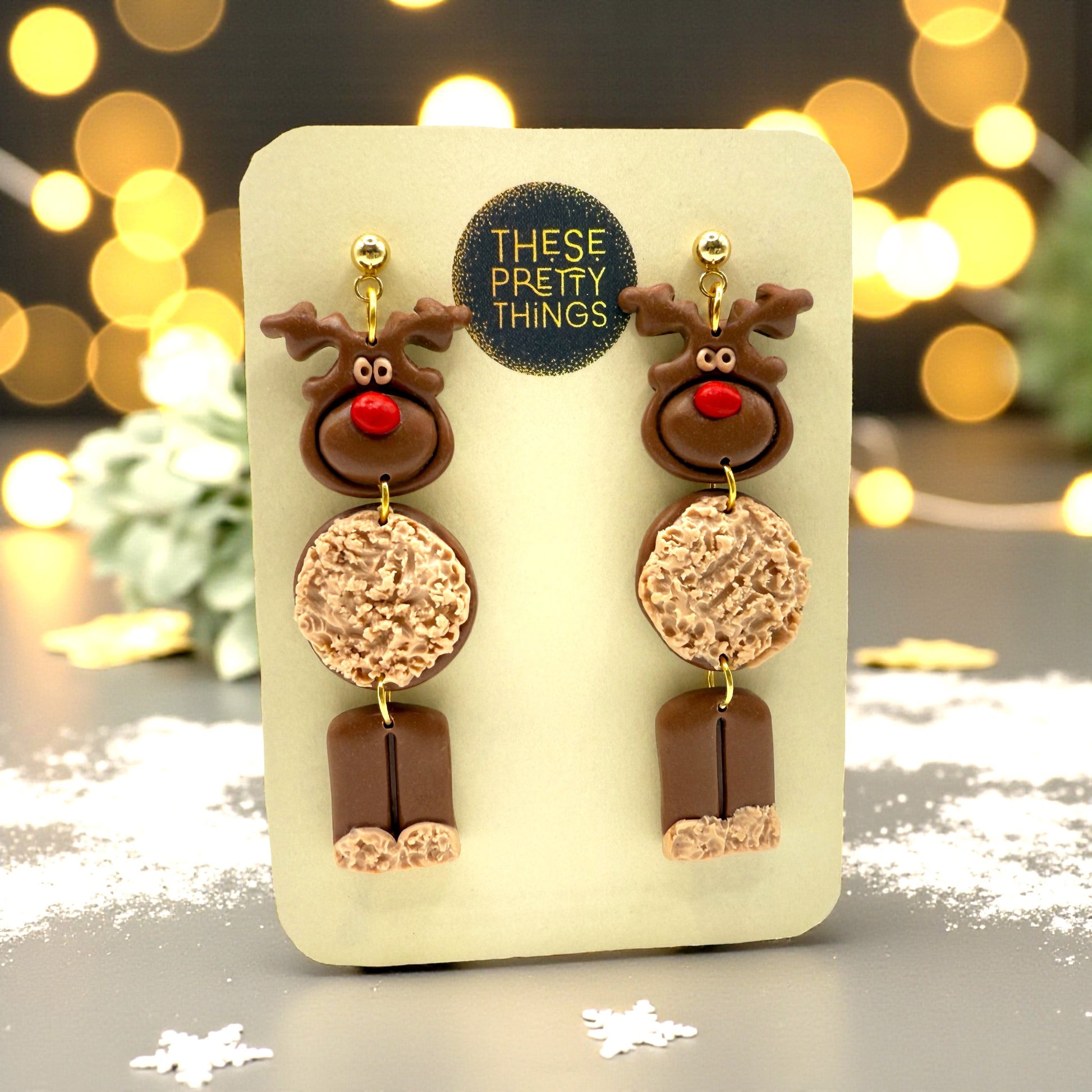 A pair of Christmas Reindeer earrings on a These Pretty Things presentation card with a festive themed background.