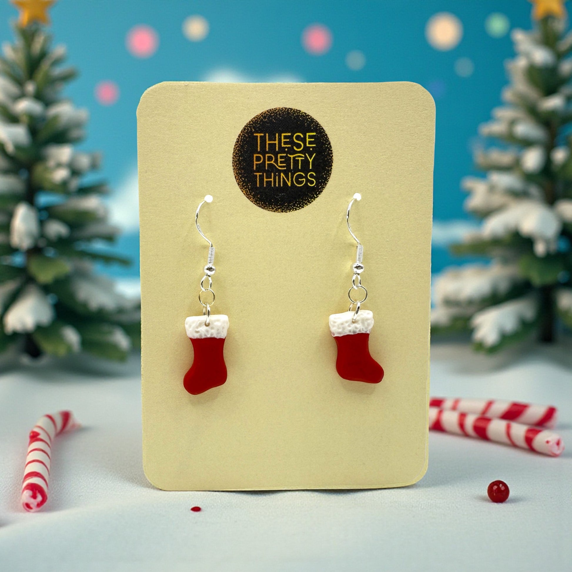 Christmas Stoclking earrings in red and white on a These Pretty Things presentation card with a festive themed backgrounc comprising of candy canes, snow and trees.