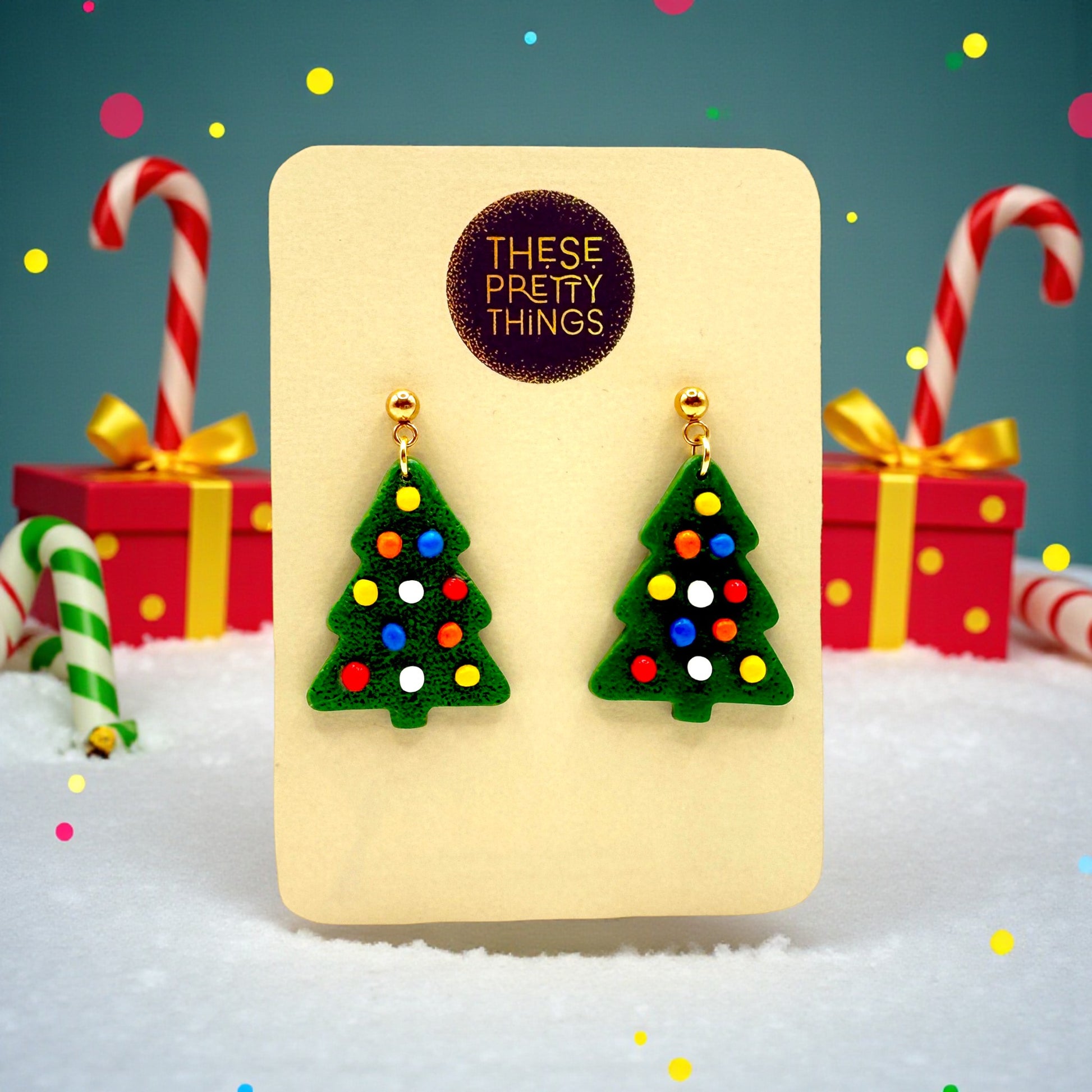 Christmas tree earrings on a 'These Pretty Things' presentation card with candy canes and gifts in the background.