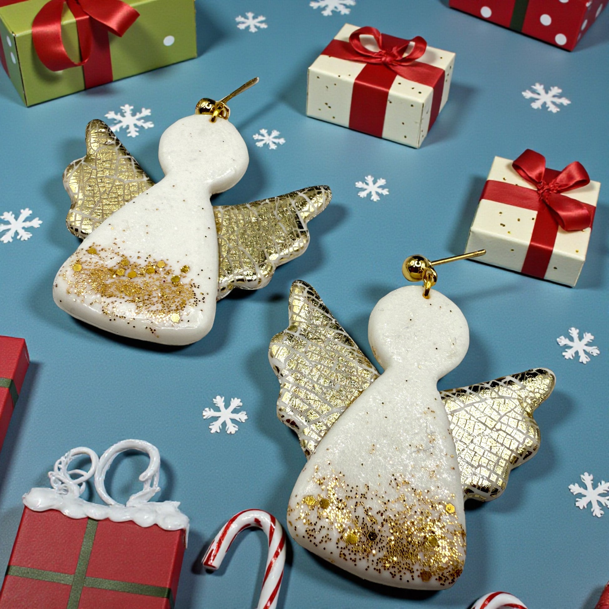 Christmas Angels earrings with gold and white glitter on a blue background with gift boxes and candy canes.