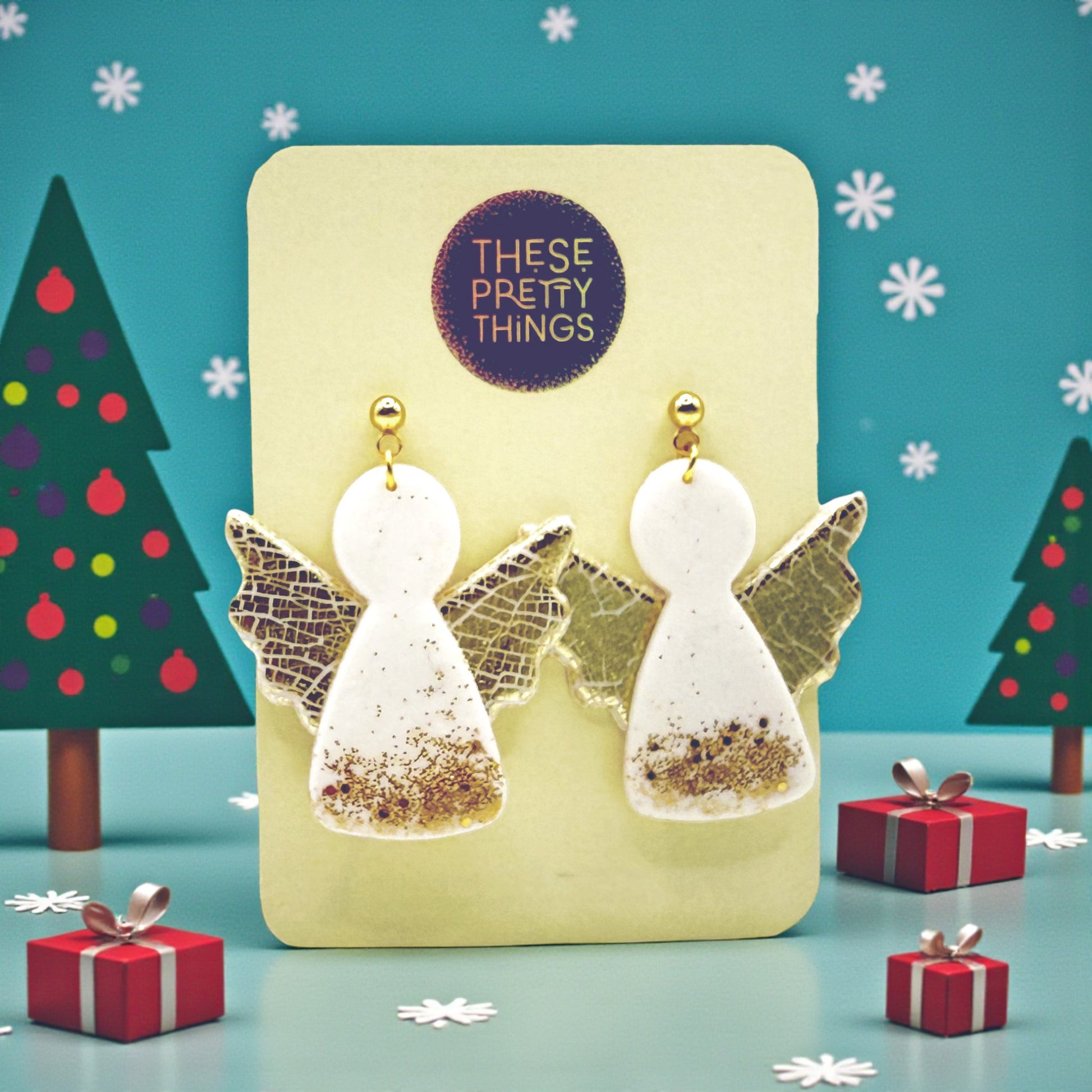 Christmas Angel earrings on a These Pretty Things presentation card with Christmas trees and presents in the background.