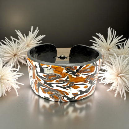 These Pretty Things Cognac Marble Cuff on a table with two creamy white feather boas either side.