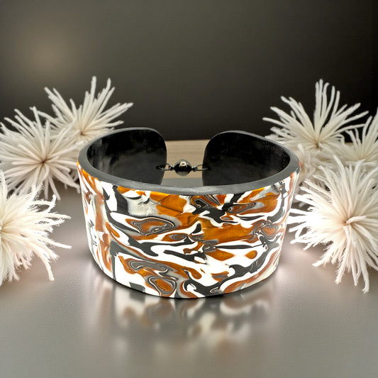 These Pretty Things Cognac Marble Cuff on a table with two creamy white feather boas either side.