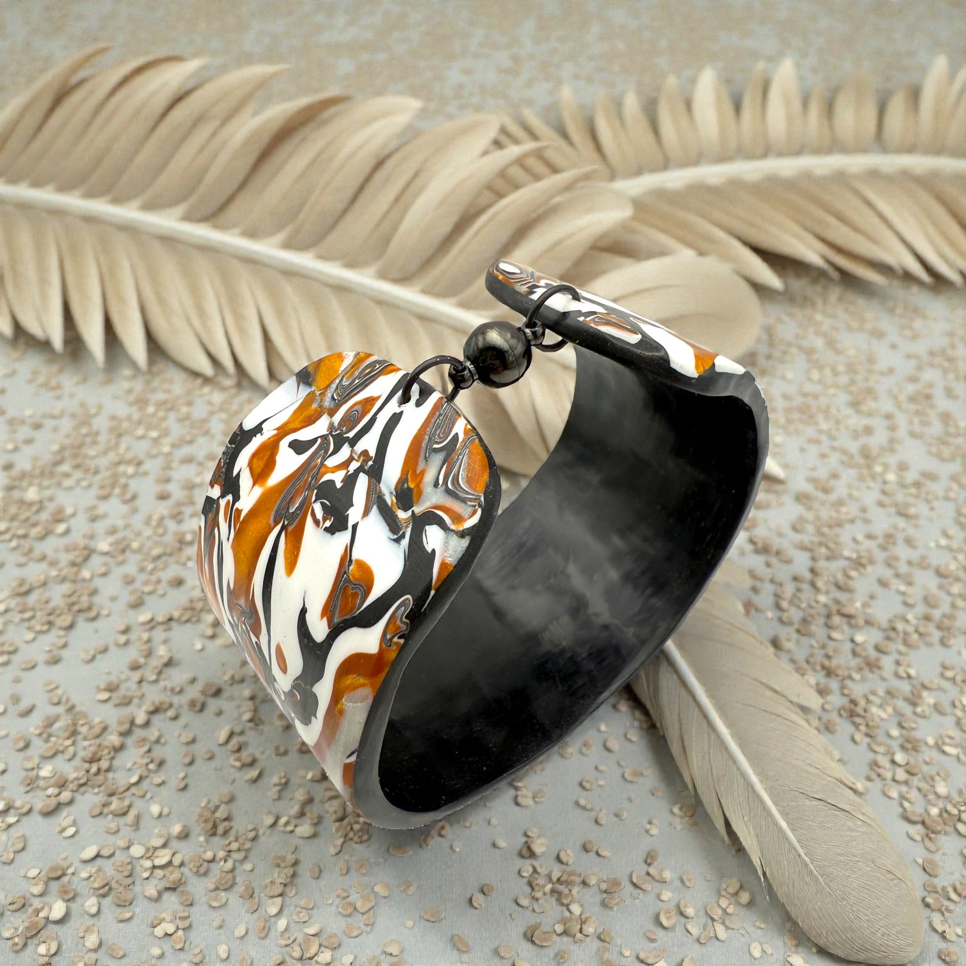 These Pretty Things Cognac Marble Cuff on a table with three creamy white feather boards framing the cuff.