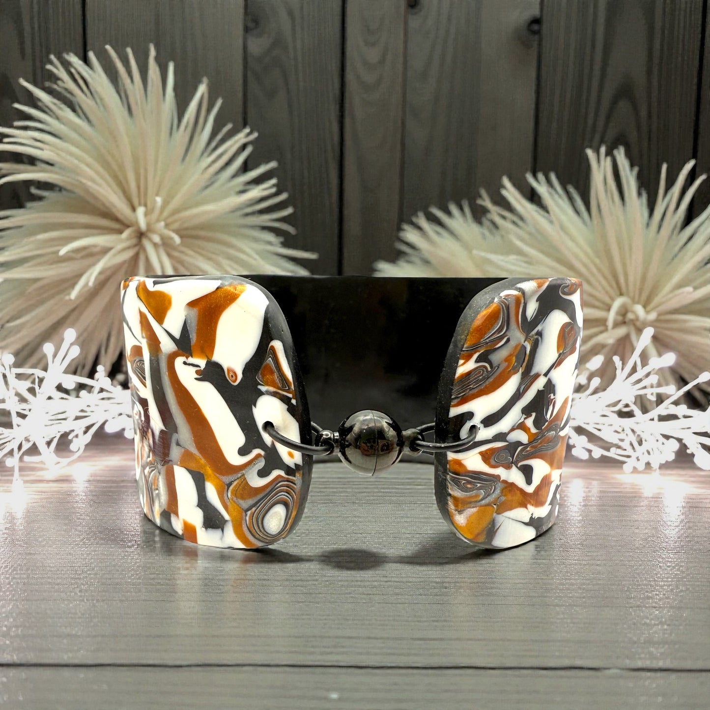 These Pretty Things Cognac Marble Cuff on a table with two creamy white feather boas either side.