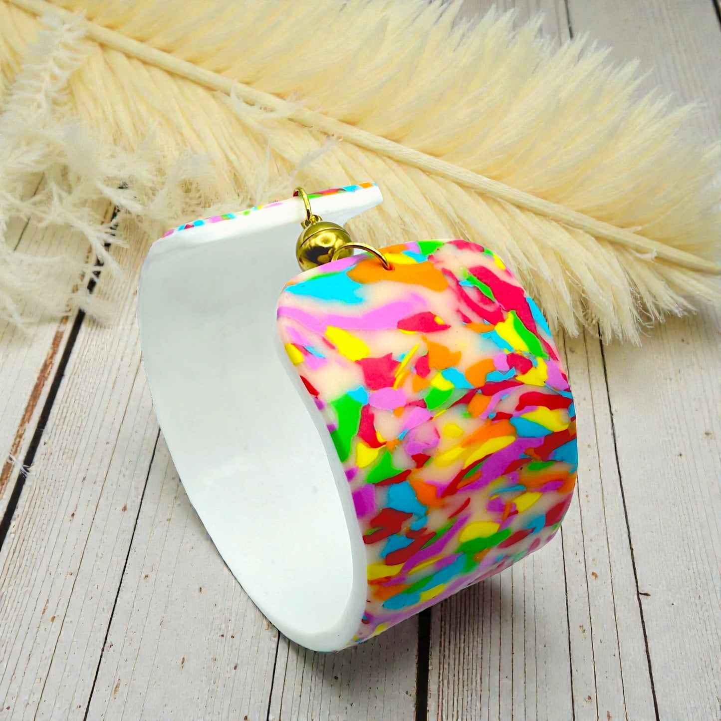These Pretty Things Confetti Cuff on a wood table with a cream feather in the background