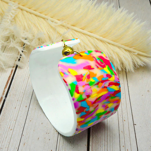 These Pretty Things Confetti Cuff on a wood table with a cream feather in the background