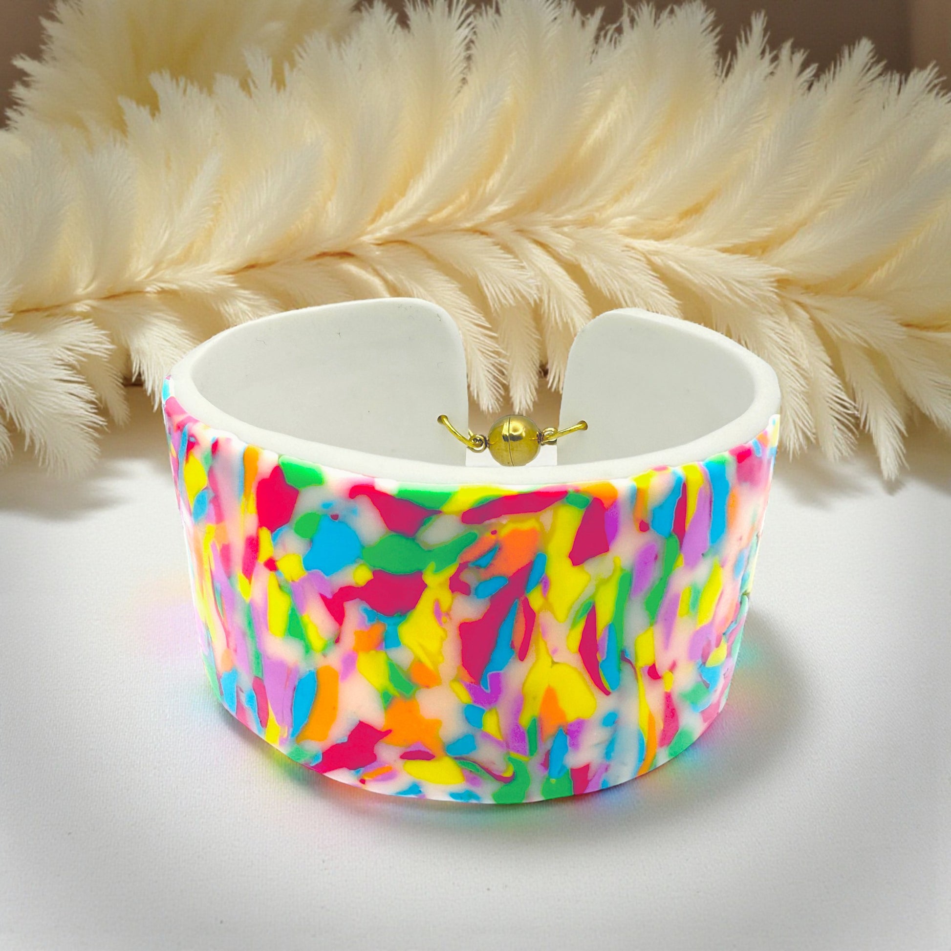 These Pretty Things Confetti Cuff on a table with a cream feather boa in the background