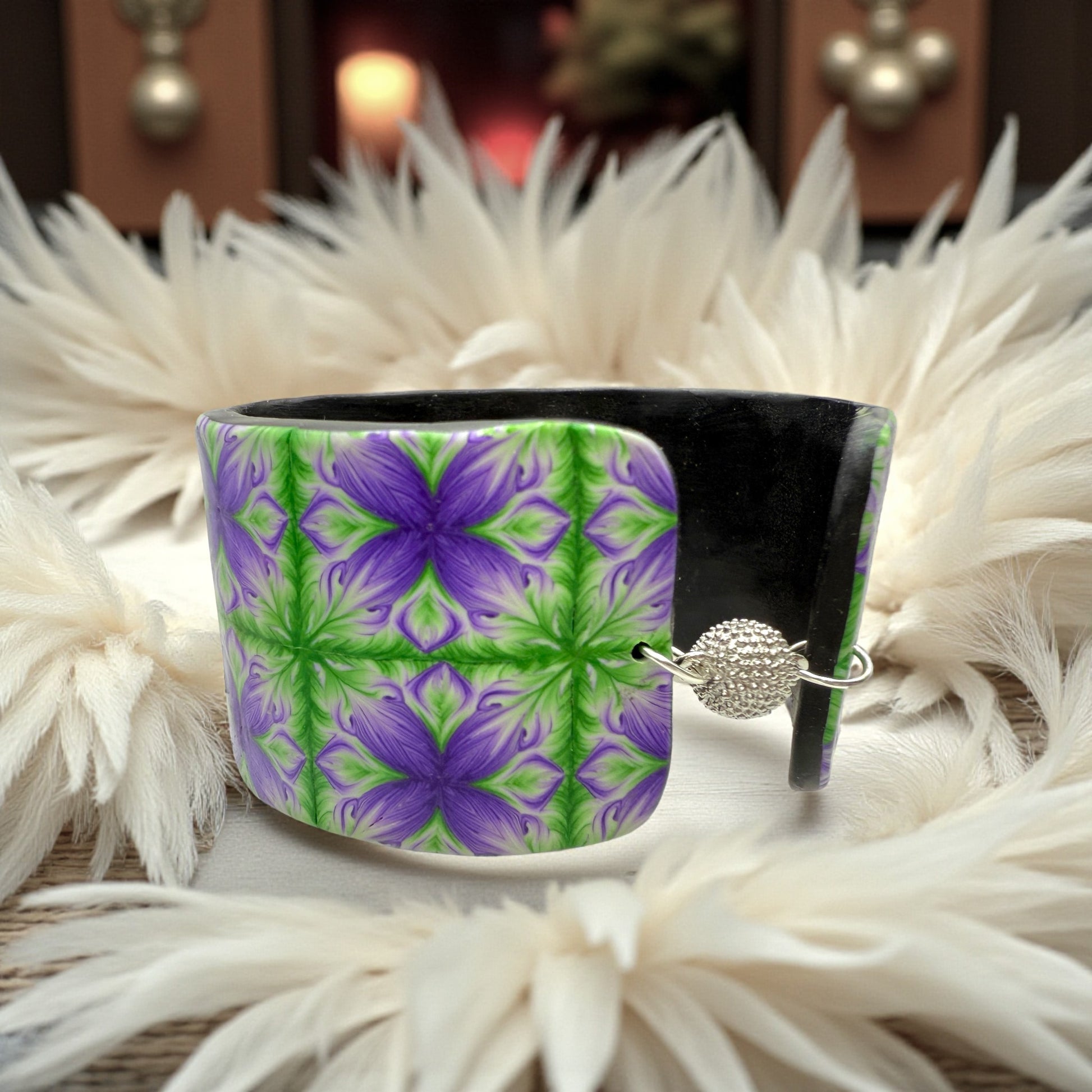 These Pretty Things Fleur De Lys Cuff with a background of a white feather boa