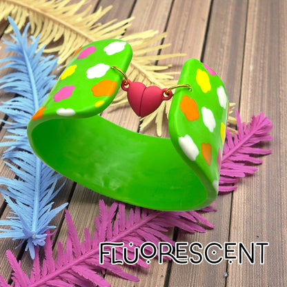 These Pretty Things Green Fluorescent Cuff on a wood slated base with coloured feathered leaves