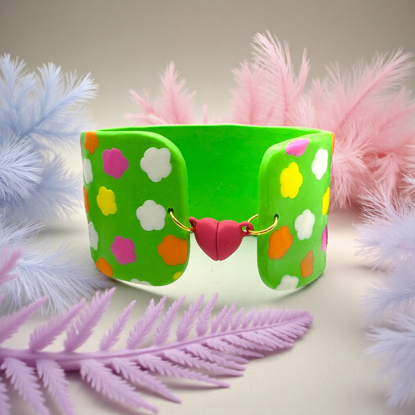 These Pretty Things Green Fluorescent Cuff on a wood slated base with coloured feathered leaves