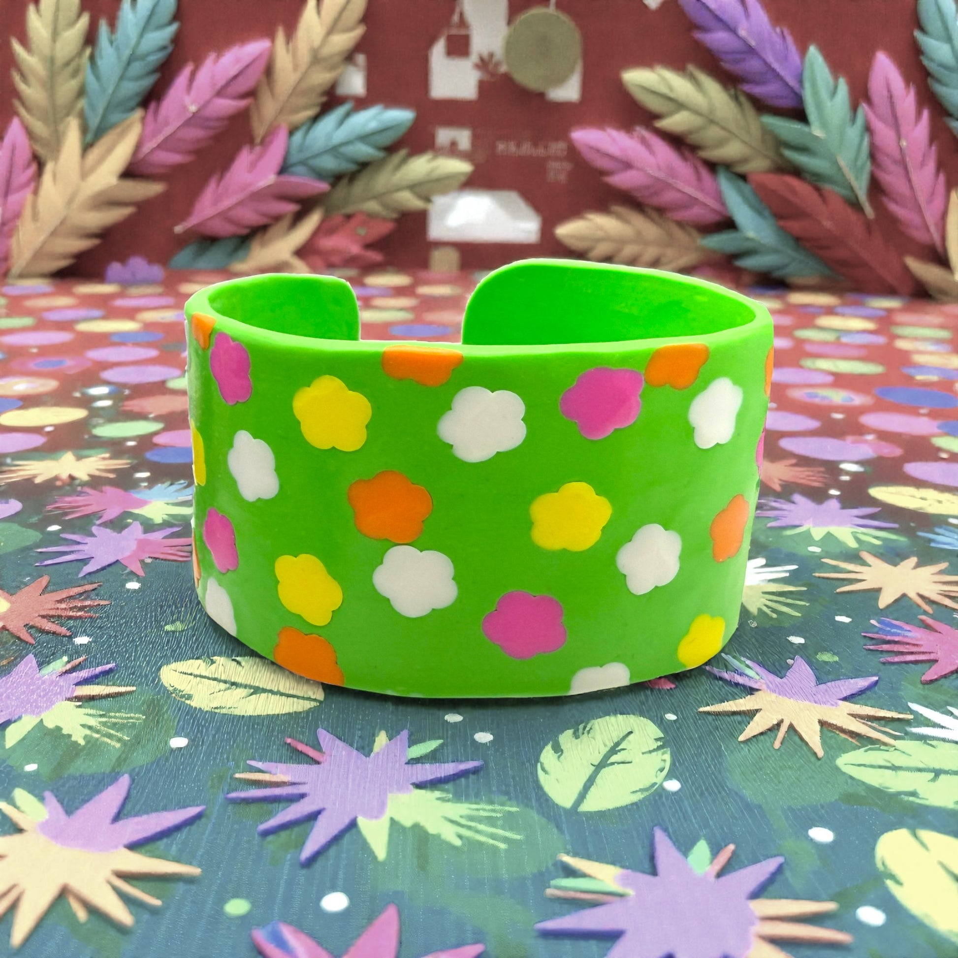 These Pretty Things Green Fluorescent Cuff on a coloured base with coloured feathered leaves