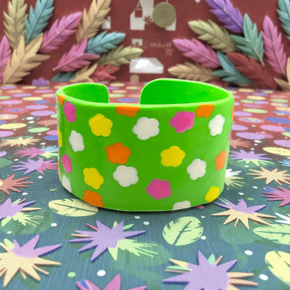 These Pretty Things Green Fluorescent Cuff on a coloured base with coloured feathered leaves