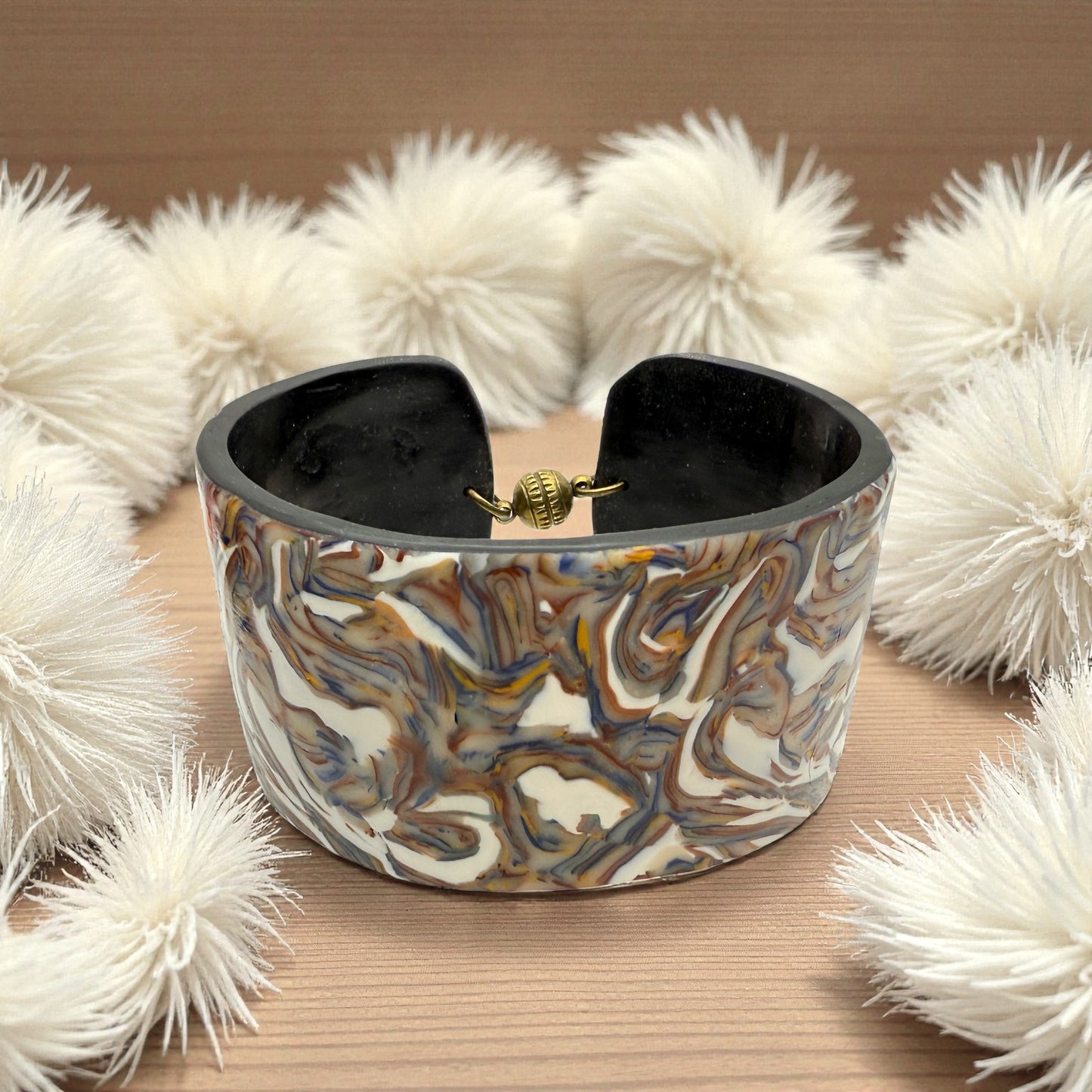 These Pretty Things Marbled Earth Cuff set in a beige feather boa on a wood grain effect table