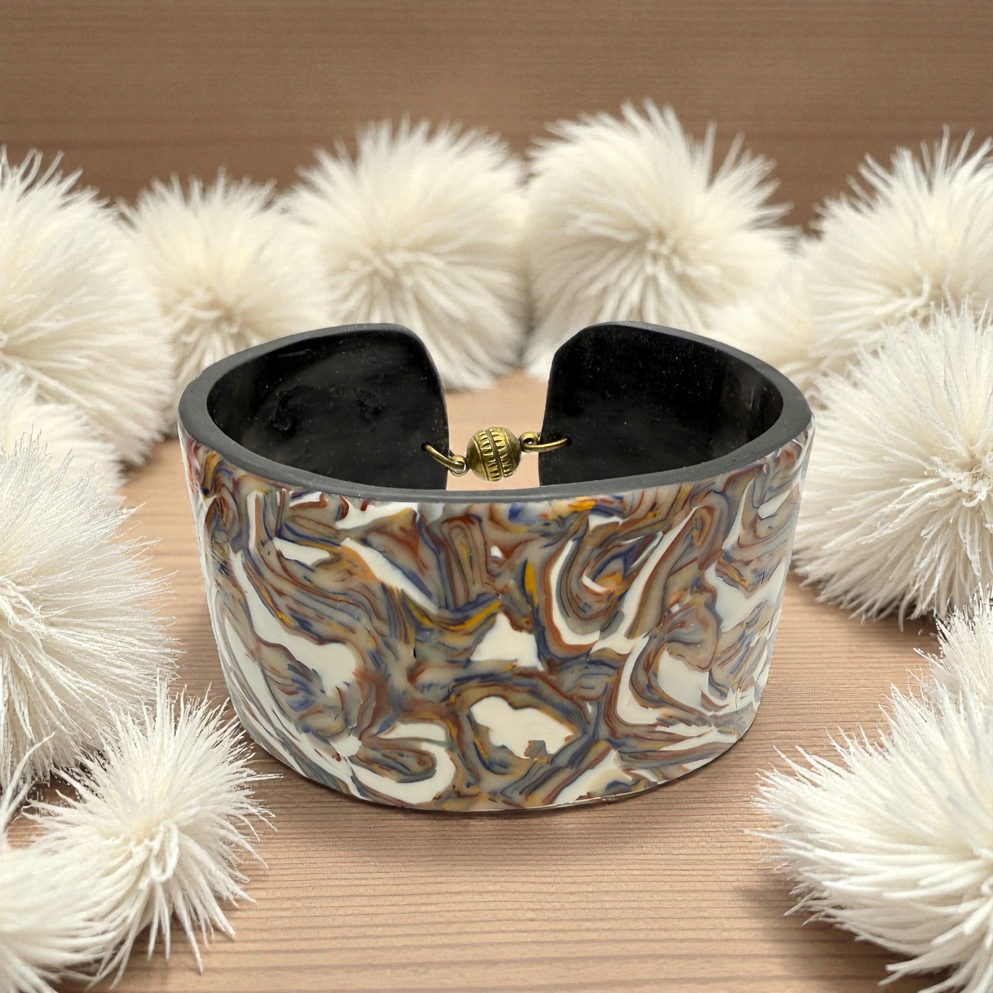 These Pretty Things Marbled Earth Cuff set in a beige feather boa on a wood grain effect table