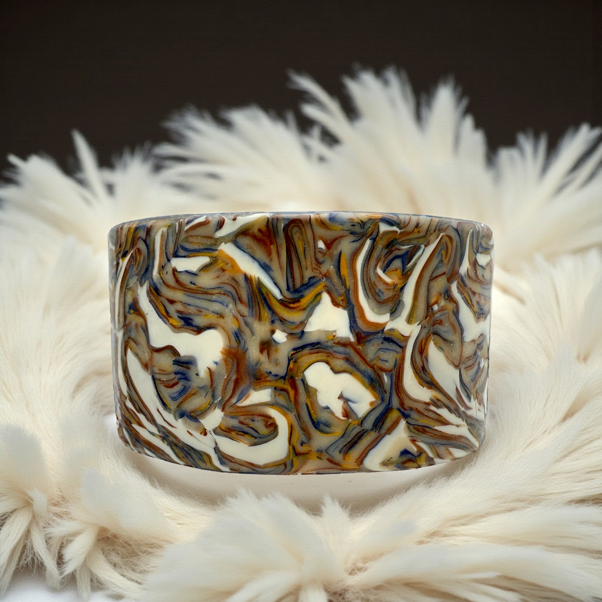 These Pretty Things Marbled Earth Cuff set in a beige feather boa on a wood grain effect table