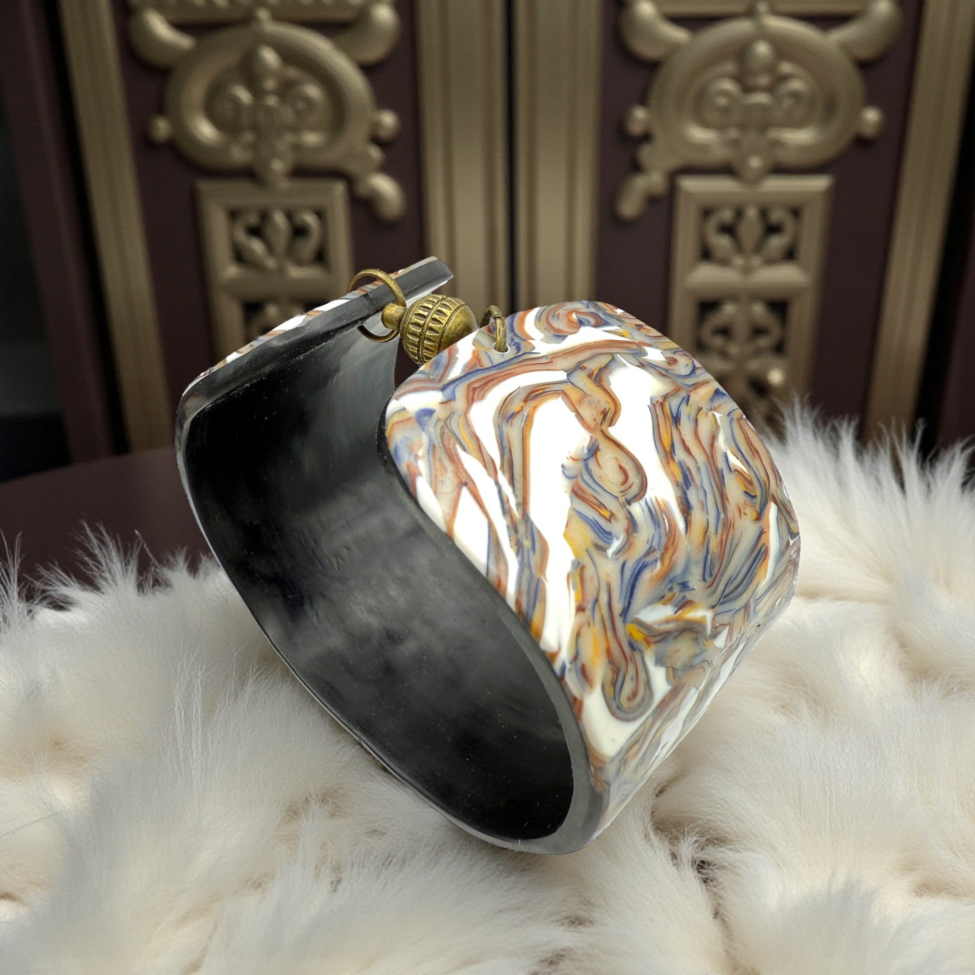 These Pretty Things Marbled Earth Cuff set in a beige feather boa on a wood table