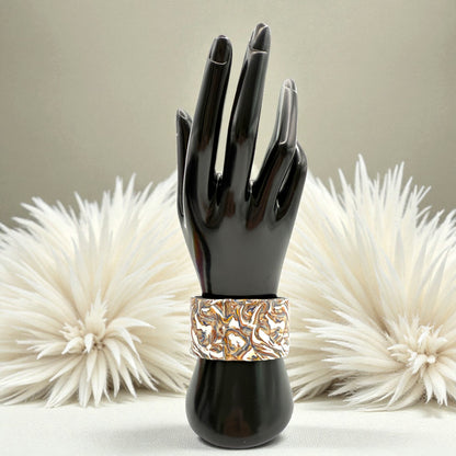 These Pretty Things Marbled Earth Cuff on a black wrist/hand demonstration bust set in front of a beige feather boa oon a beige colour table