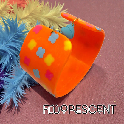 These Pretty Things Orange Fluorescent Cuff on a muted pink base with blue and yellow feather boas in the background