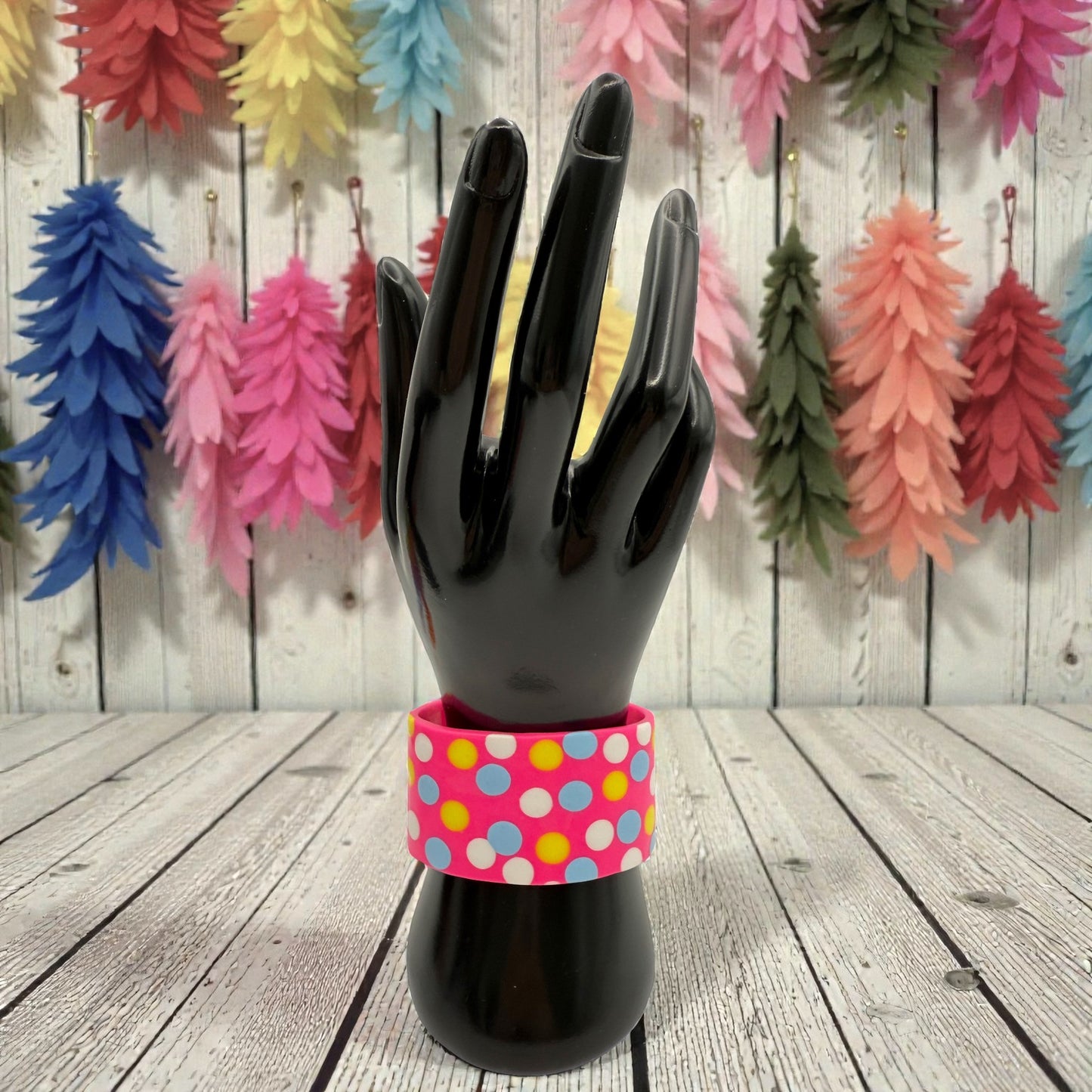 These Pretty Things Pink Fluorescent Cuff on a black hand mannequin with a variety of pale coloured feathers in the background