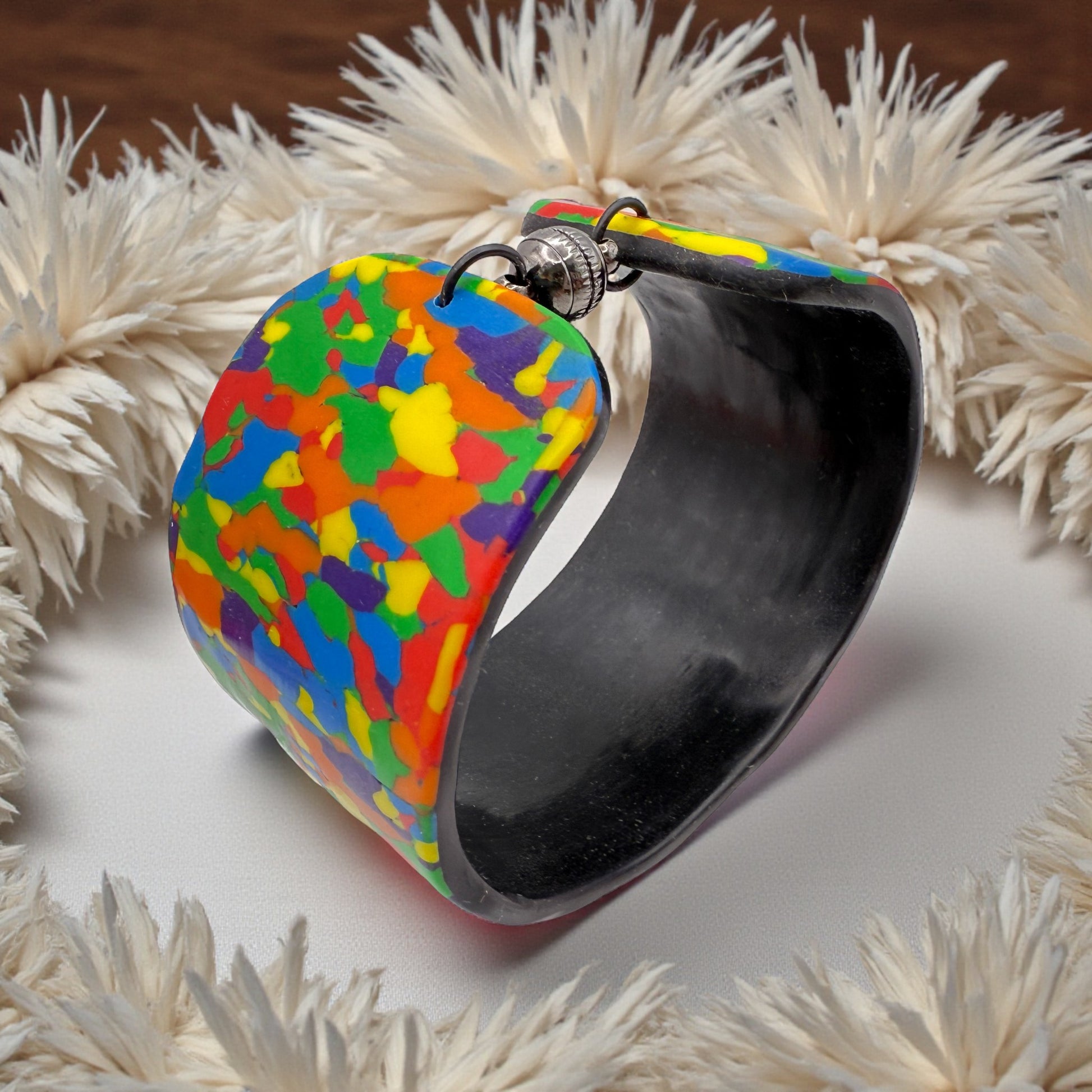 These Pretty Things Pixel Party Cuff on a neutral table with a beige feather boa in the background